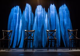 Na scenie cztery krzesła . Za nimi, podświetlona na niebiesko kotara.