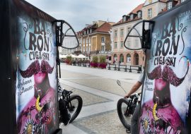 Dwa mobilne rowery reklamowe z plakatami firmującymi spektakl ''Baron cygański''. W tle Rynek Kościuszki w Białymstoku.